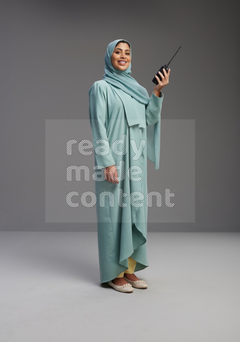 Saudi Woman wearing Abaya standing holding walkie-talkie on Gray background