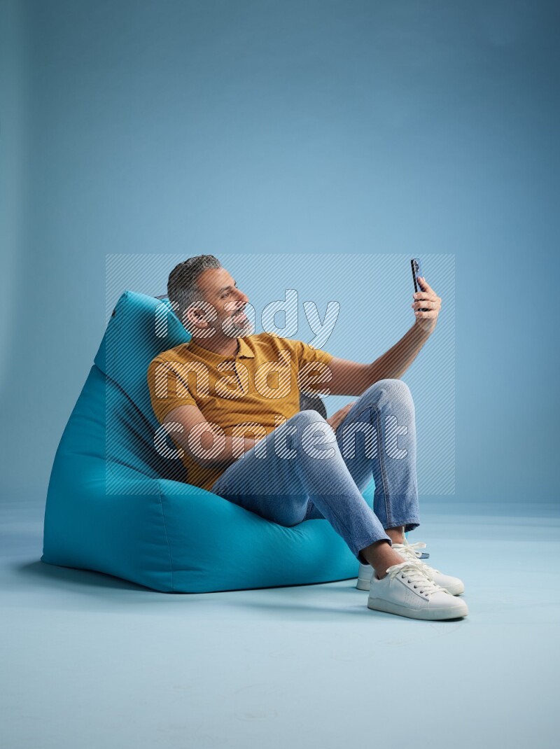 A man sitting on a blue beanbag and taking selfie