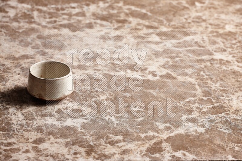 A beige pottery bowl on beige marble background