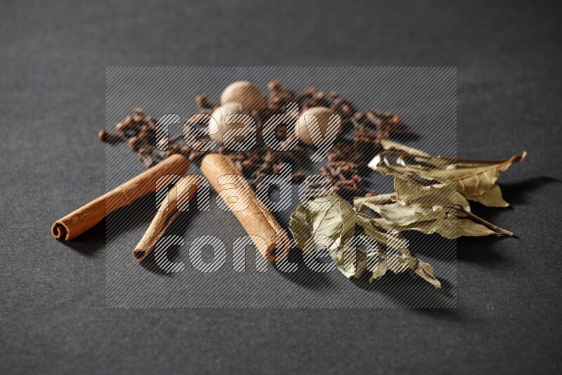 Cloves, ginger, bay laurel and cinnamon sticks on black flooring