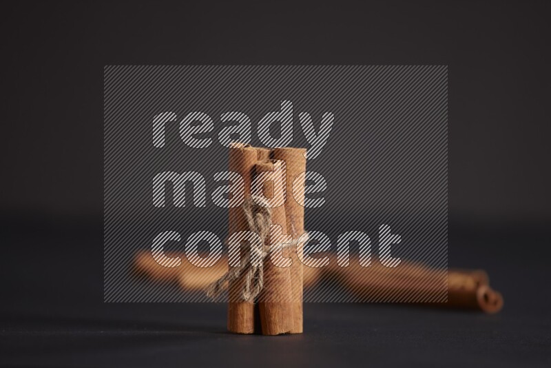 4 Cinnamon sticks stacked and bounded with more sticks in the background on black flooring