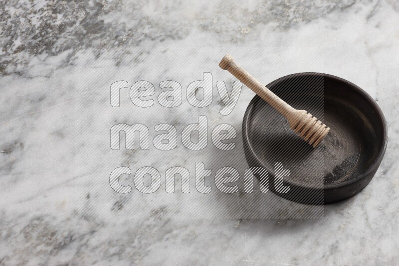 Black pottery oven plate with wooden honey dipper in it on grey marble background