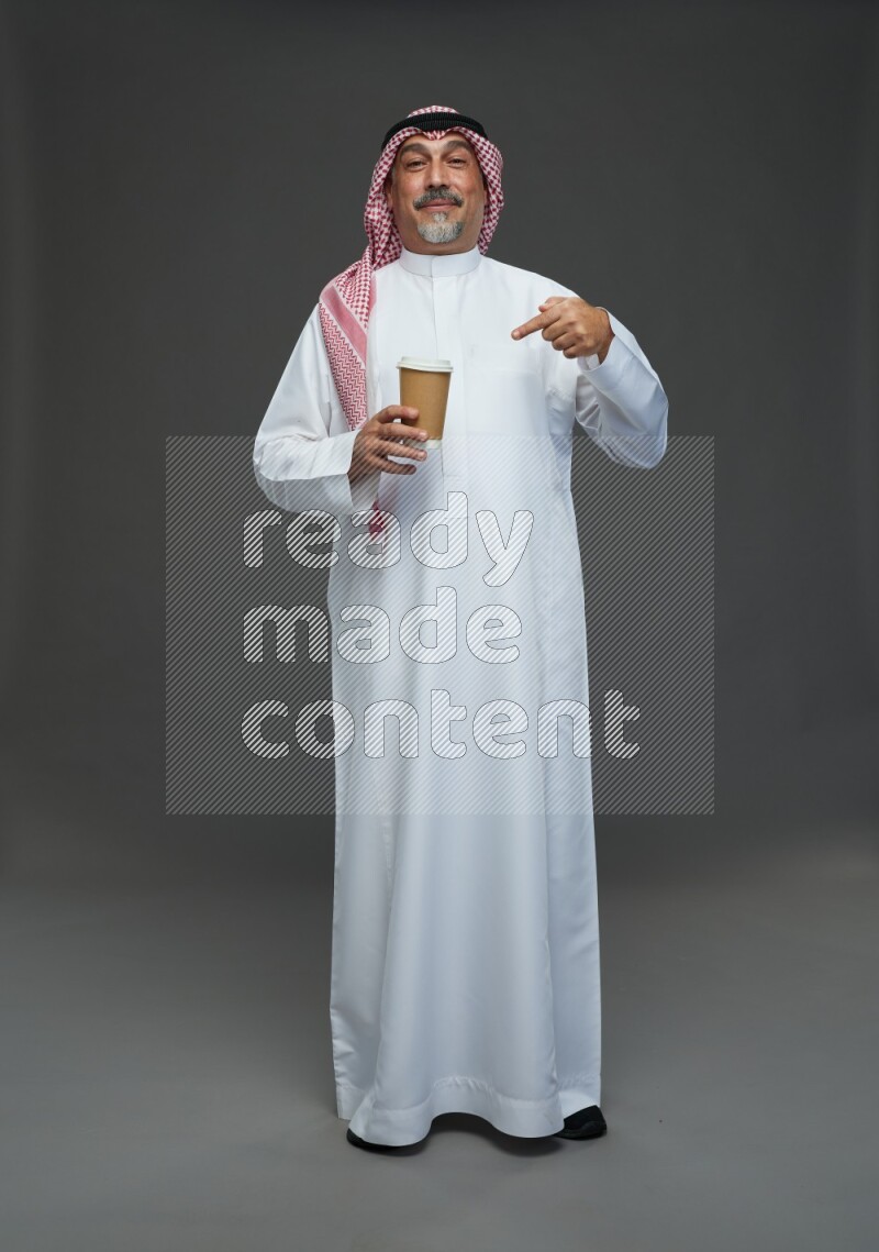 Saudi man with shomag Standing holding paper cup on gray background