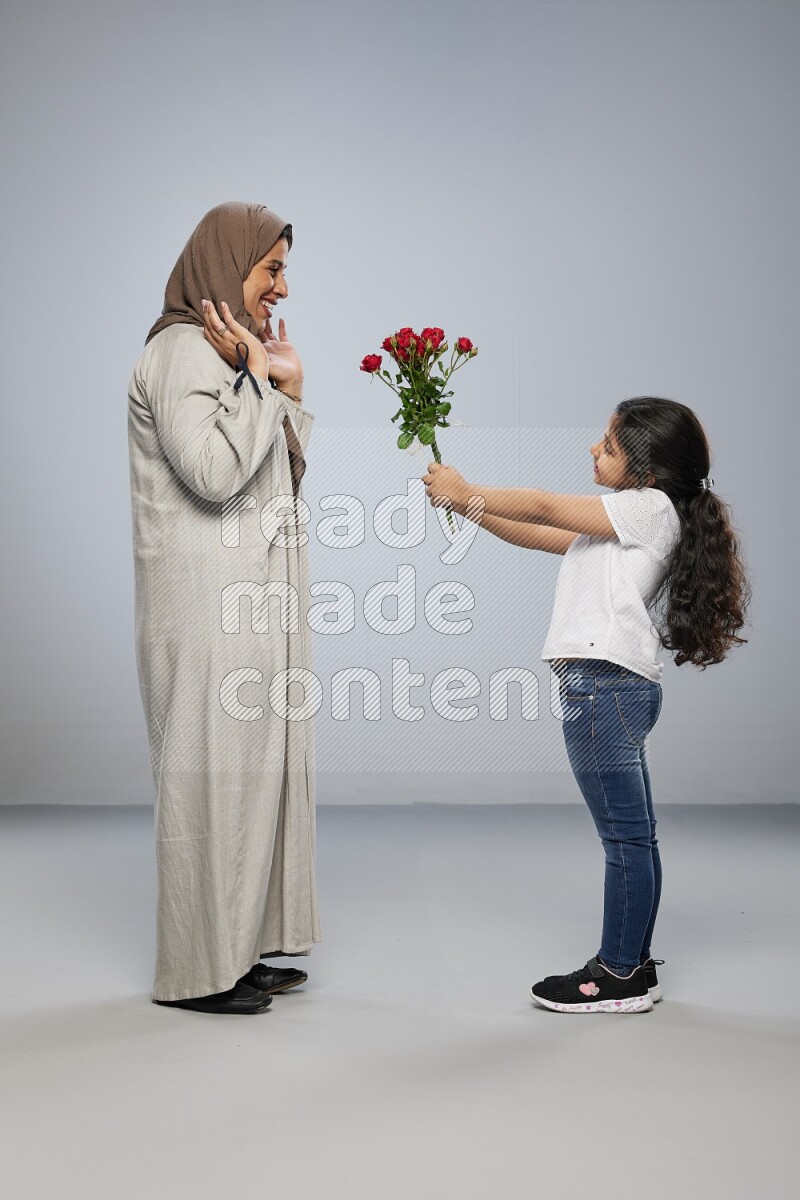 A girl standing giving flowers to her mother on gray background