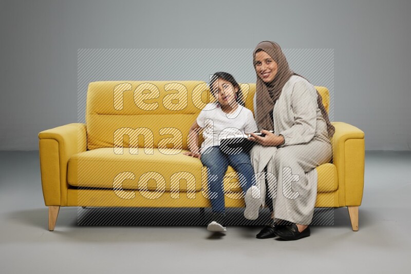 Mom and daughter sitting reading a book on gray background