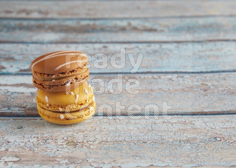 45º Shot of of two assorted Brown Irish Cream, and Yellow Piña Colada macarons on light blue background