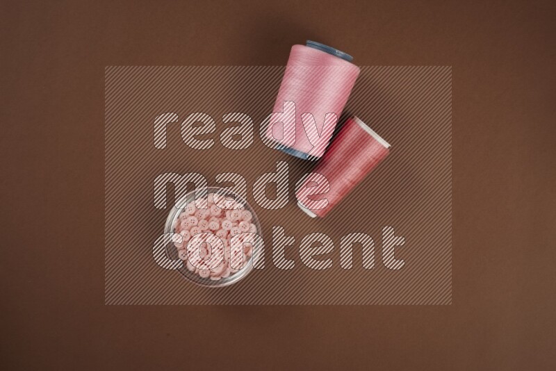 A pink collection of sewing and tailoring tools arranged on a brown background