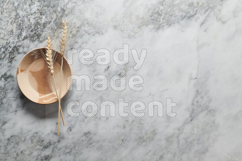 Wheat stalks on multicolored pottery plate on grey marble background