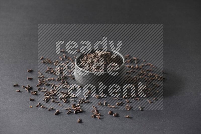 A black pottery bowl full of cloves on a black flooring