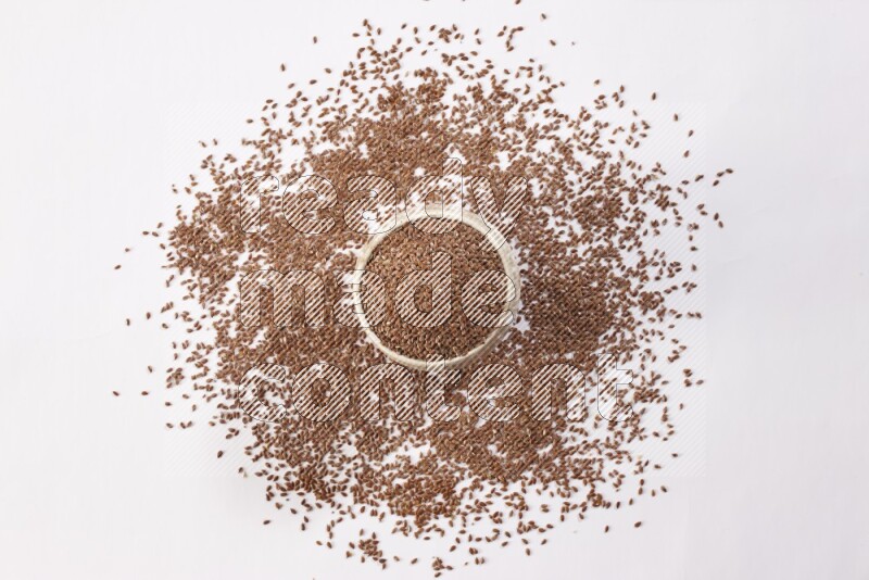 وعاء بيج فخاري ممتلئ بحبوب بذر الكتان مع بعض الحبوب المتناثرة علي خلفية بيضاء