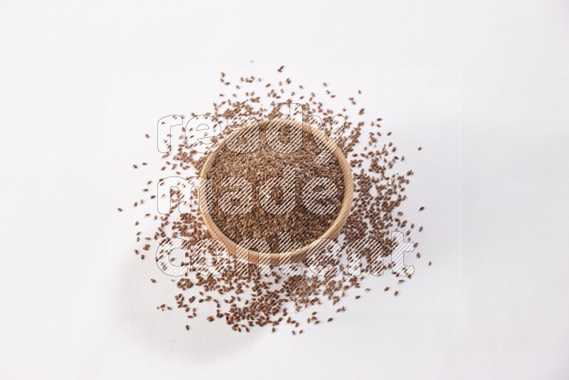 وعاء خشبي ممتلئ بحبوب بذر الكتان ومحاط بالبذور علي خلفية بيضاء