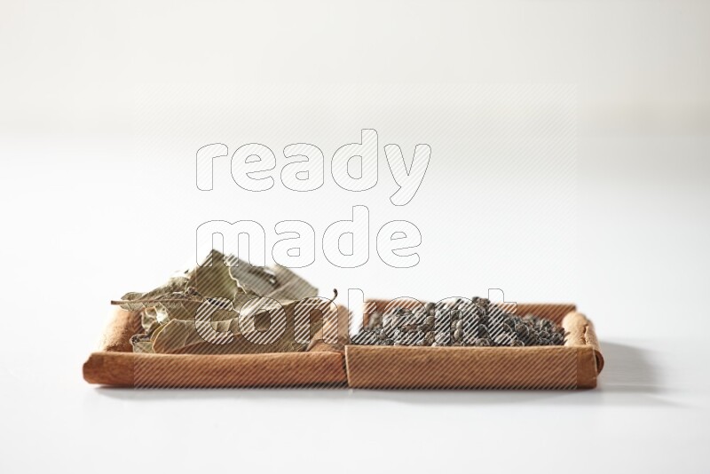 مربعان من أعواد القرفة ممتلئان بحبوب الفلفل الأسود وأوراق الغار علي خلفية بيضاء