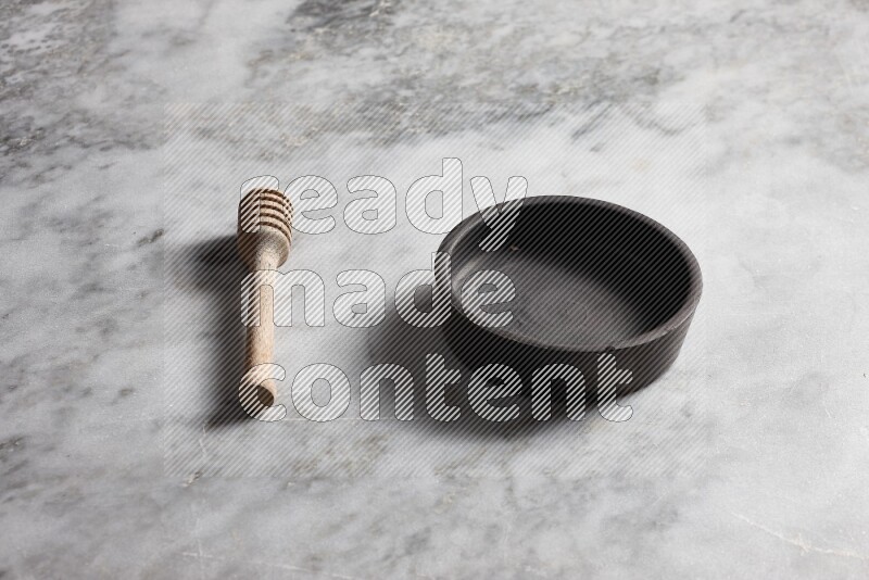 Black pottery bowl with wooden honey dipper on the side on grey marble background