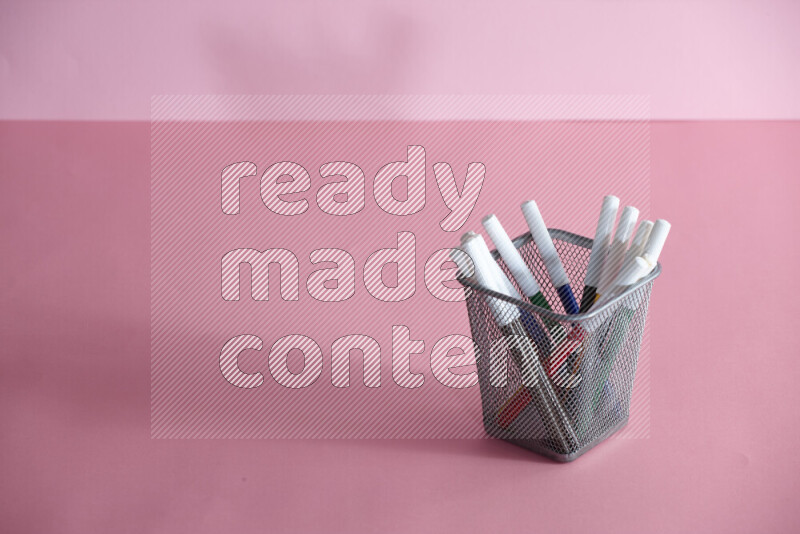 Pens, pencils and other different school supplies in a metal pen holder on rose background