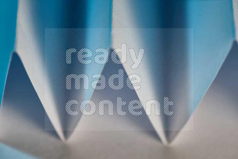 A close-up abstract image showing sharp geometric paper folds in white and blue gradients
