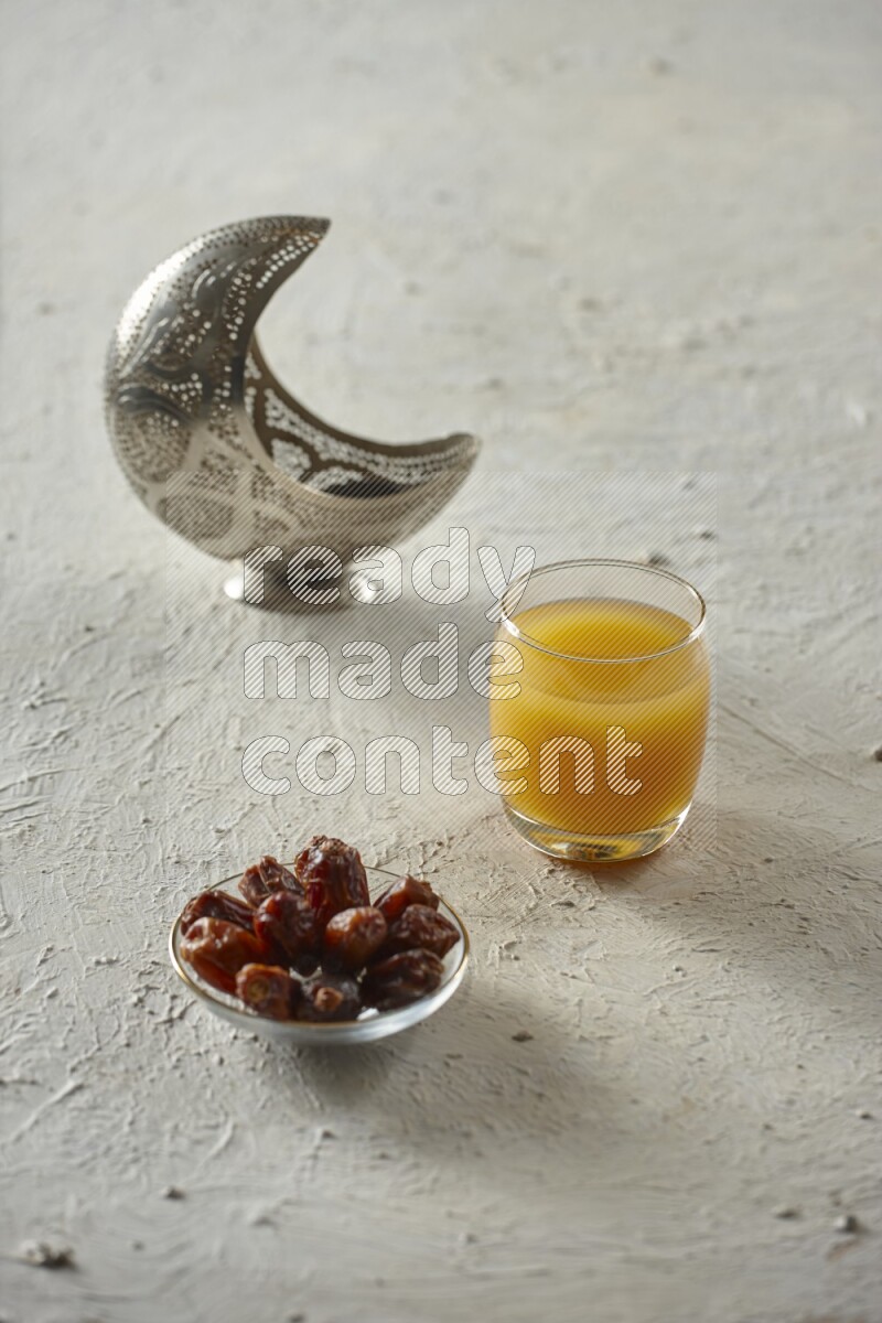 A silver lantern with different drinks, dates, nuts, prayer beads and quran on textured white background