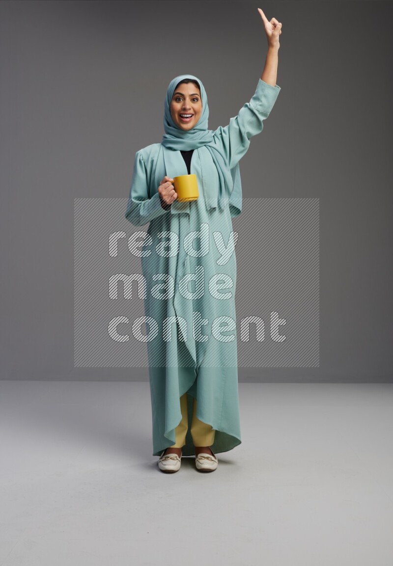 Saudi Woman wearing Abaya standing  holding a mug on Gray background