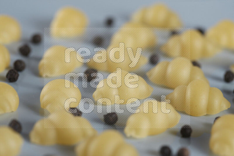 Raw pasta with different ingredients such as cherry tomatoes, garlic, onions, red chilis, black pepper, white pepper, bay laurel leaves, rosemary, cardamom and mushrooms on light blue background