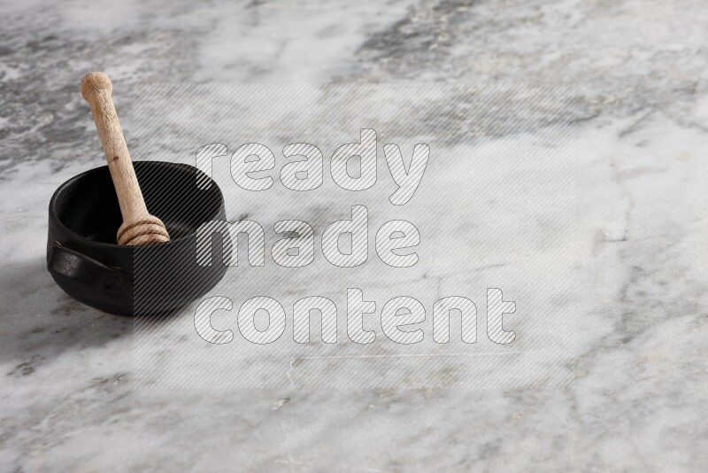 وعاء فخاري أسود مع ملعقة عسل خشبية بداخله على خلفية من الرخام الرمادي