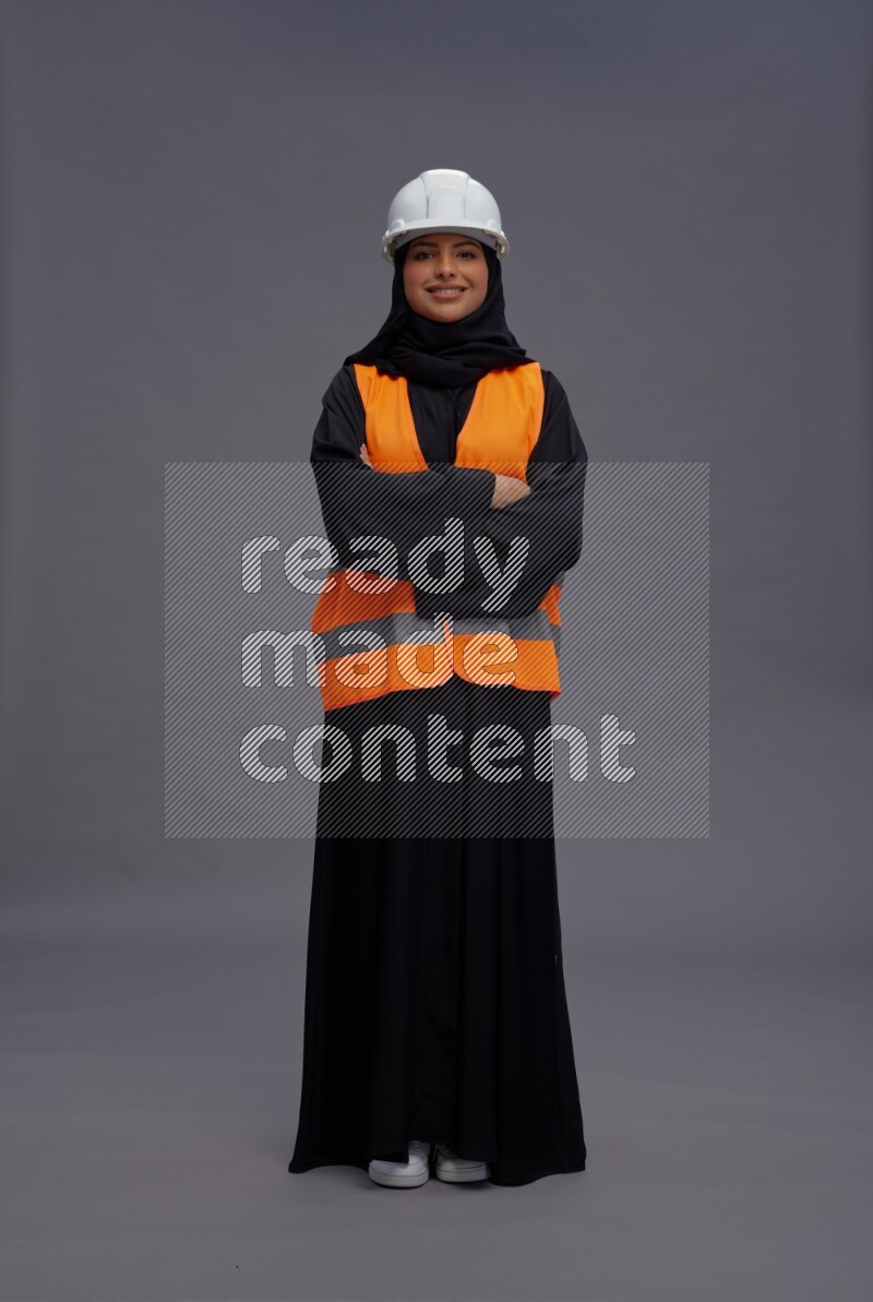 Saudi woman wearing Abaya with engineer vest standing with crossed arms on gray background