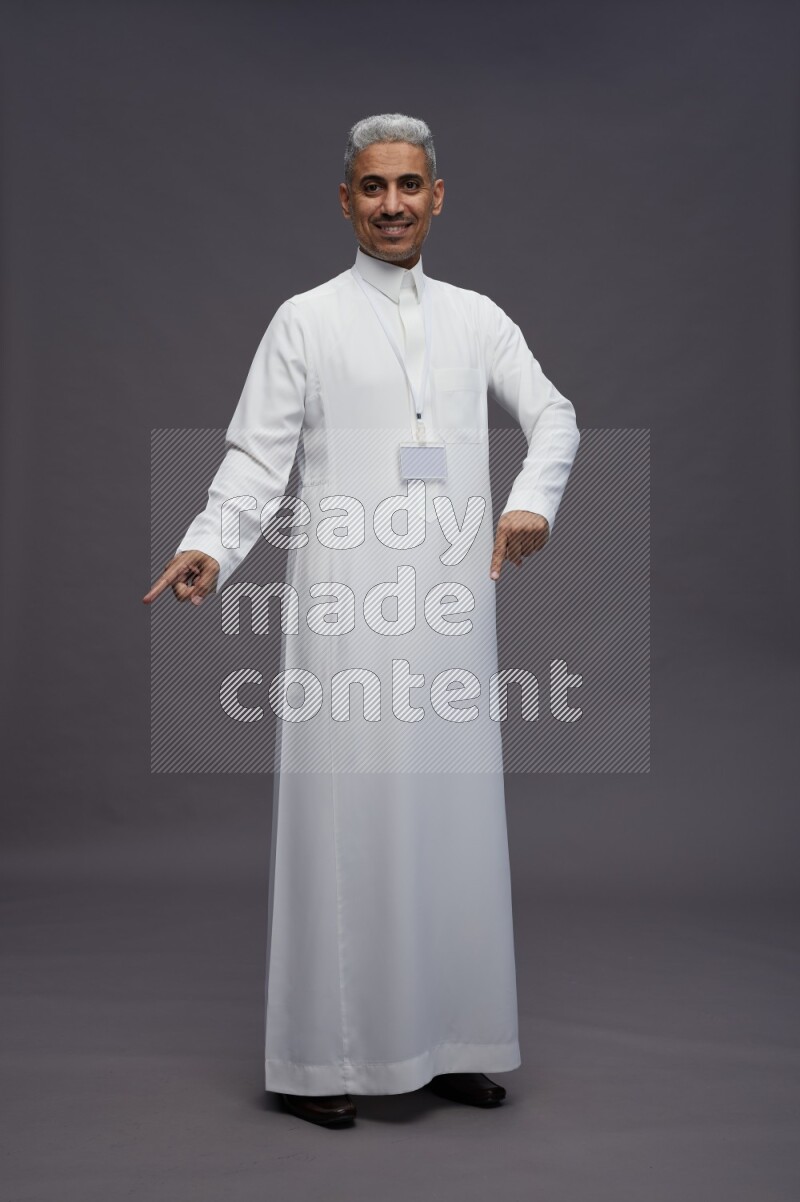 Saudi man wearing thob with neck strap employee badge standing interacting with the camera on gray background