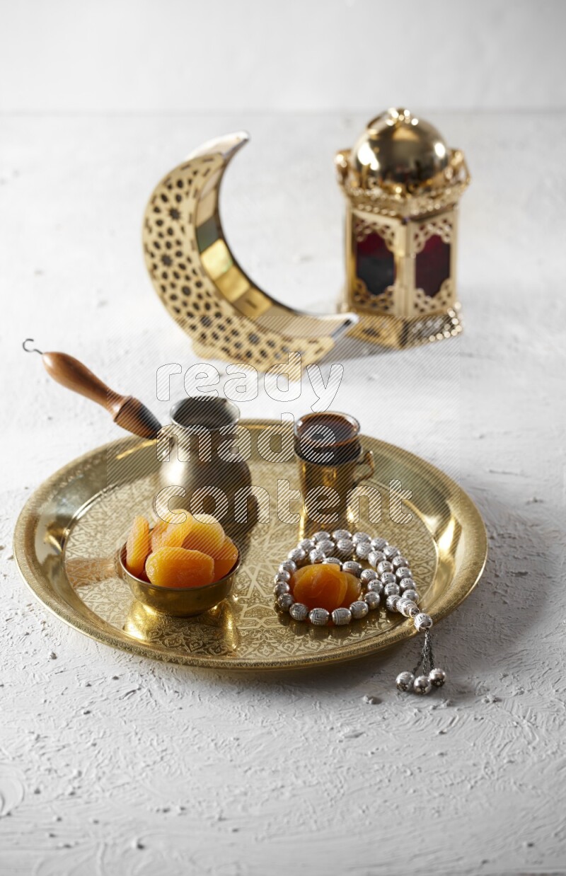 Dried apricots in a metal bowl with coffee and prayer beads on a tray beside lanterns in a light setup