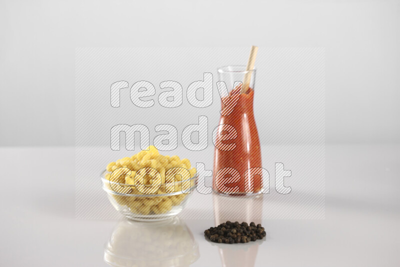 Raw pasta with tomatoe pasta with different ingredients such as cherry tomatoes, basil, garlic, bay laurel, cardamom, white pepper, black pepper, red chilis and wheat stalks on light grey background