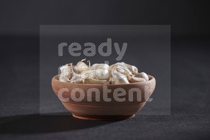 A wooden bowl full of garlic cloves on a black flooring