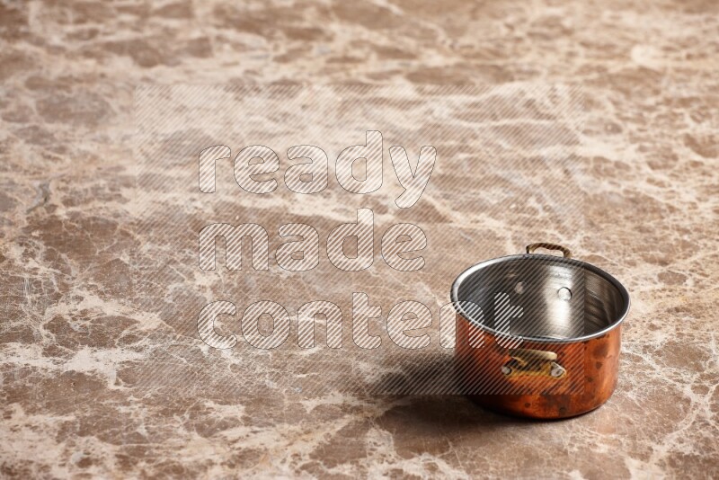 A small copper pot on beige marble background