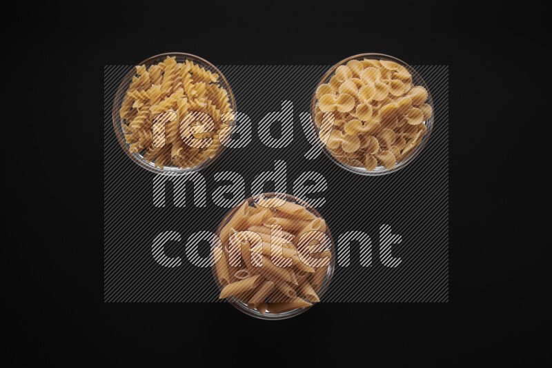 Different pasta types in glass bowls on black background