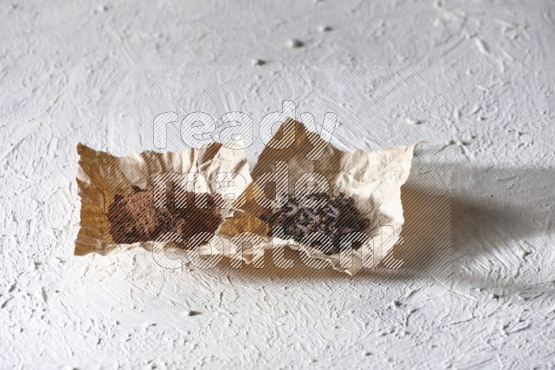 Cloves powder and cloves on 2 crumpled pieces of paper on a textured white flooring