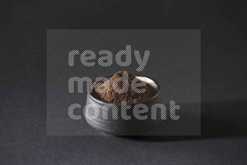 A black pottery bowl full of cloves powder on a black flooring