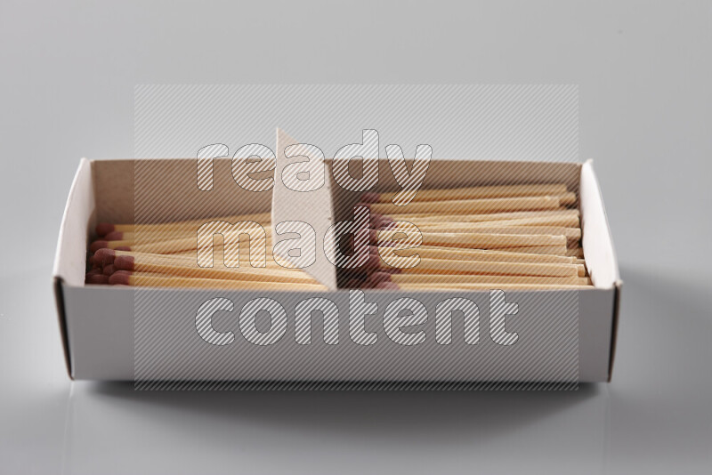 An open matchbox revealing wooden matches on a grey background