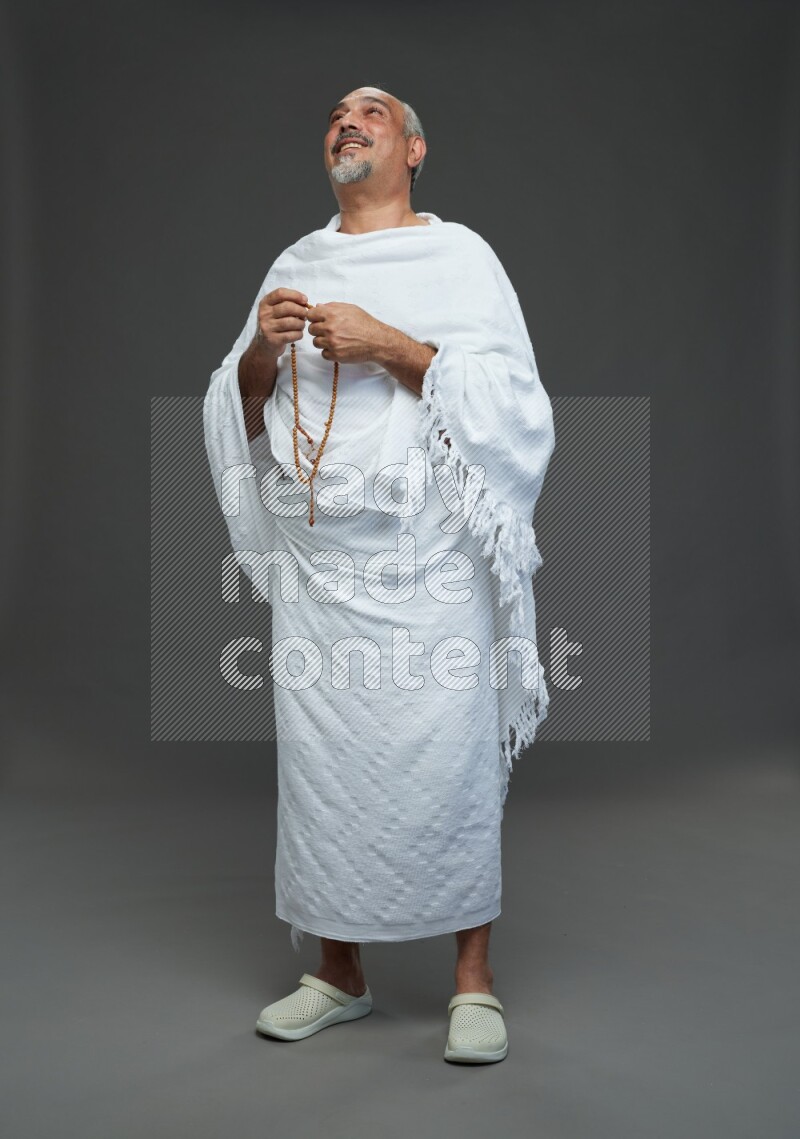 A man wearing Ehram Standing holding rosary on gray background