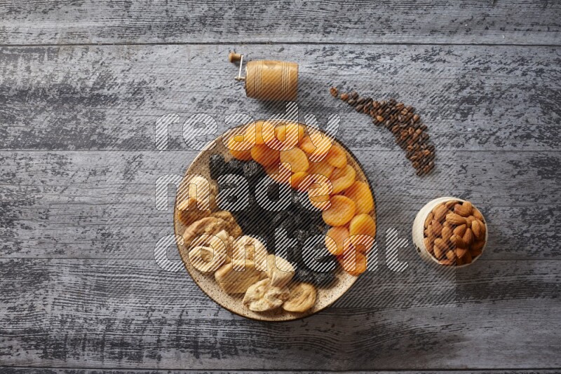 Dried fruits in a pottery plate with nuts and coffee in a dark setup