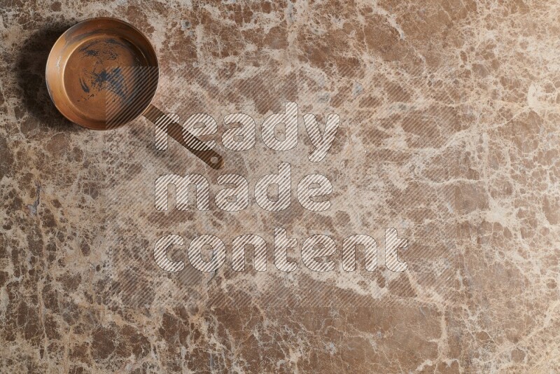 A small copper pan on beige marble background