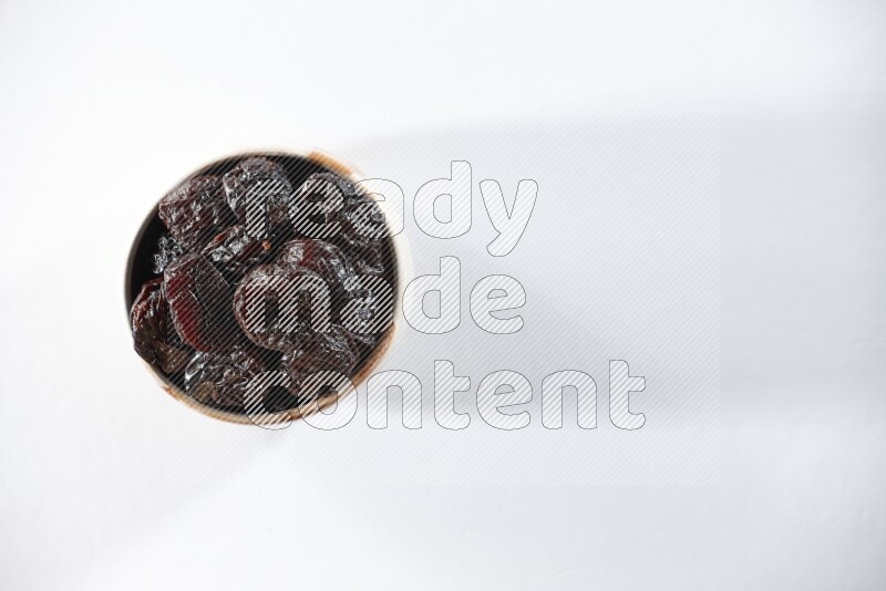 A beige ceramic bowl full of dried plums on a white background in different angles