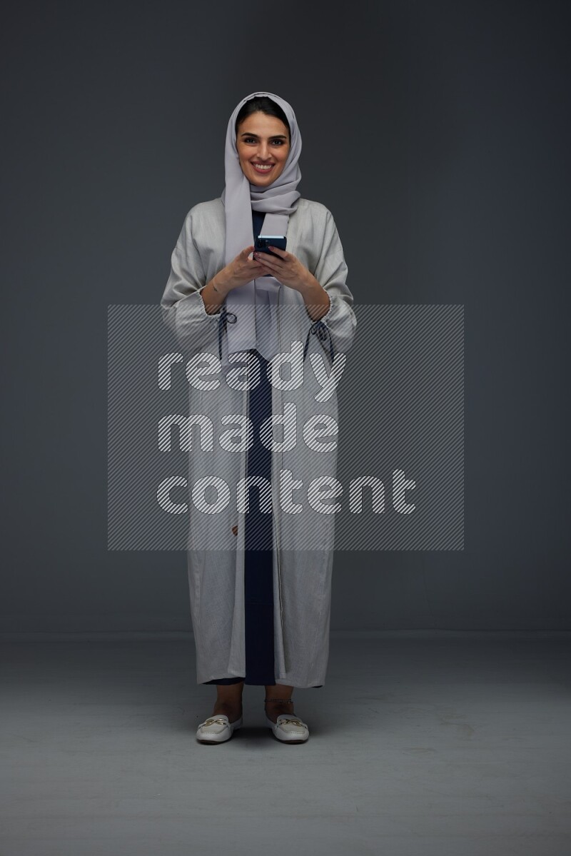 A Saudi woman Texting wearing Grey Abaya on a grey background
