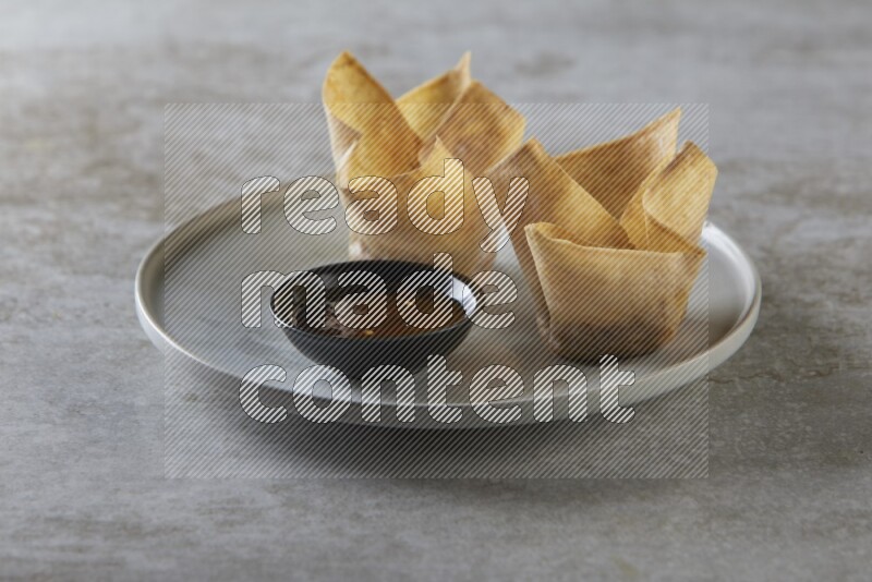 wonton cups with soy sauce ramkin on grey ceramic plate on grey textured counter top