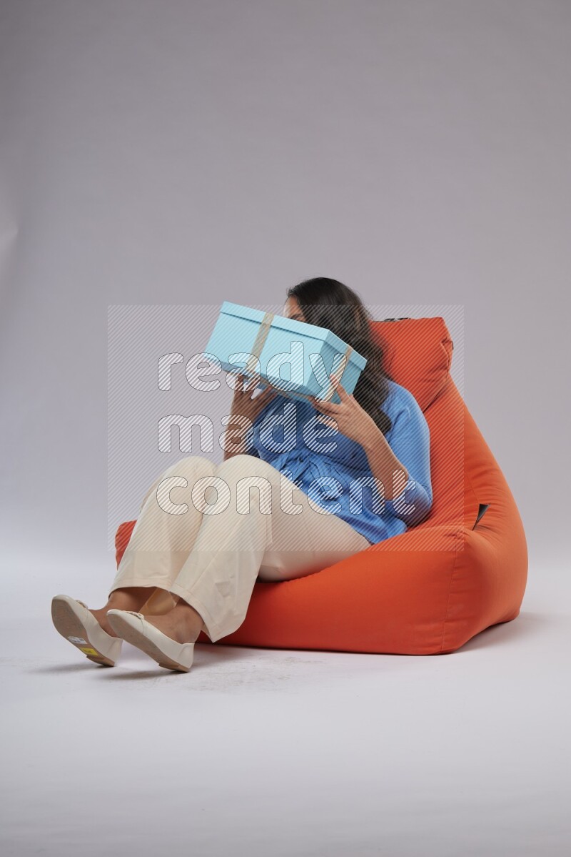A woman sitting on an orange beanbag and opining a gift
