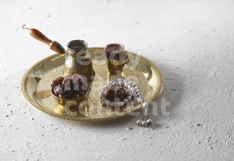 Dates in a metal bowl with coffee and prayer beads on a tray in a light setup