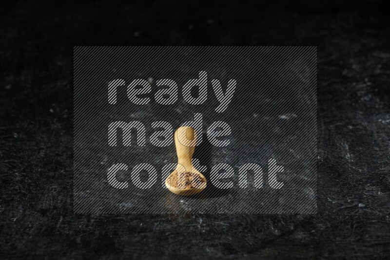 A wooden spoon full of allspice powder on a textured black flooring