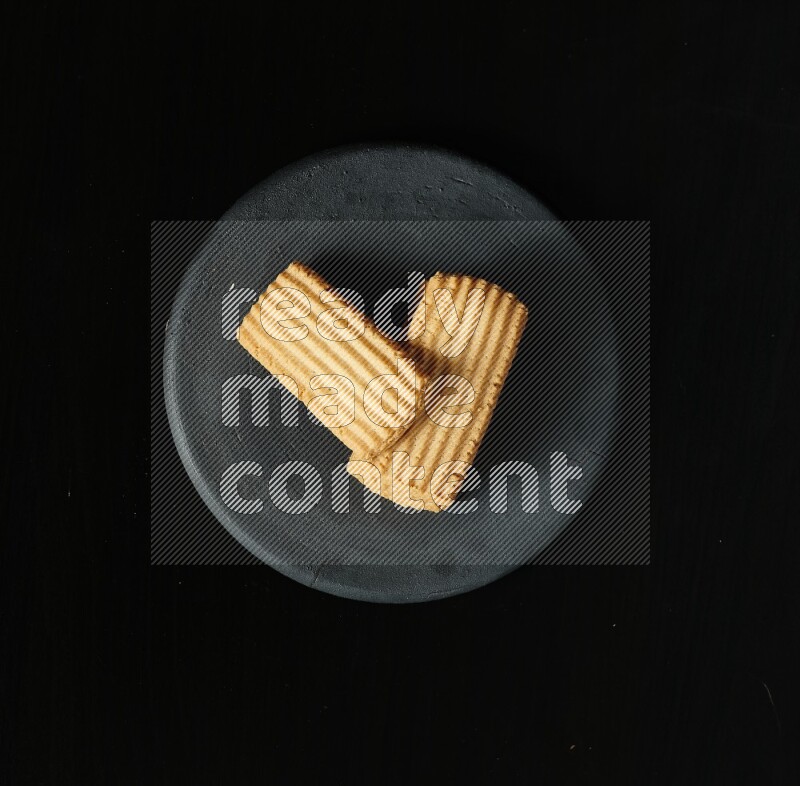 Golden biscuits in a black pottery plate on black background