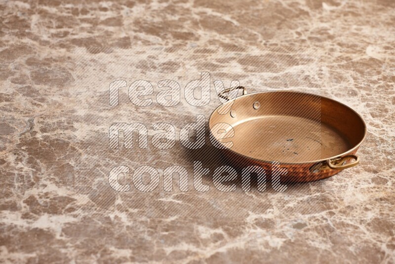 A small copper pan on beige marble background