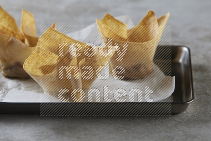 wonton cups on parchment paper in stainless tray on grey textured counter top