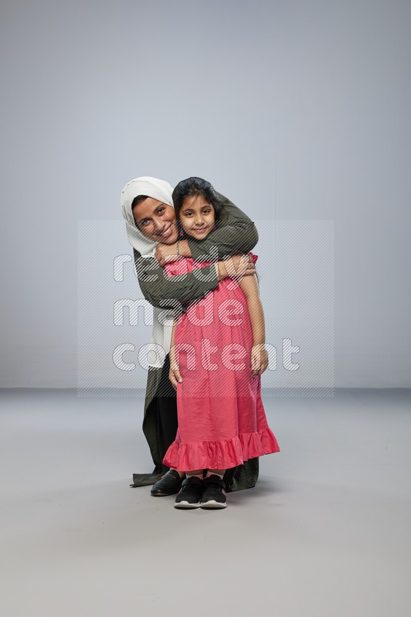 A girl and her mother interacting with the camera on gray background