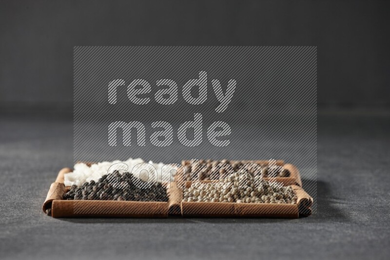 4 مربعات من عيدان القرفة ممتلئة بحبوب الفلفل الأسود والفلفل الأبيض وبهار الفلفل الحلو والملح الأبيض على أرضية سوداء