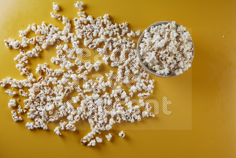 A white pottery bowl full of popcorn with popcorn beside it on a yellow background in different angles