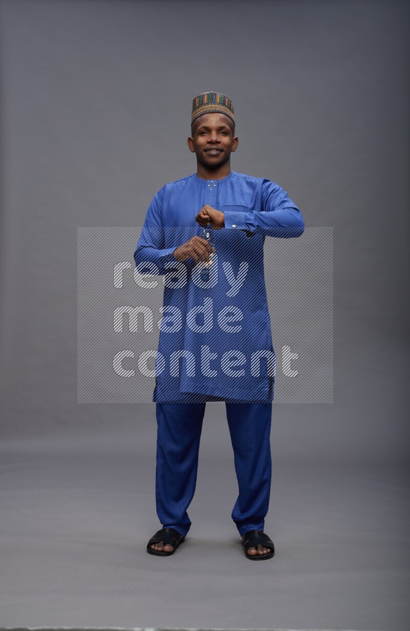 Man wearing Nigerian outfit standing drinking water on gray background