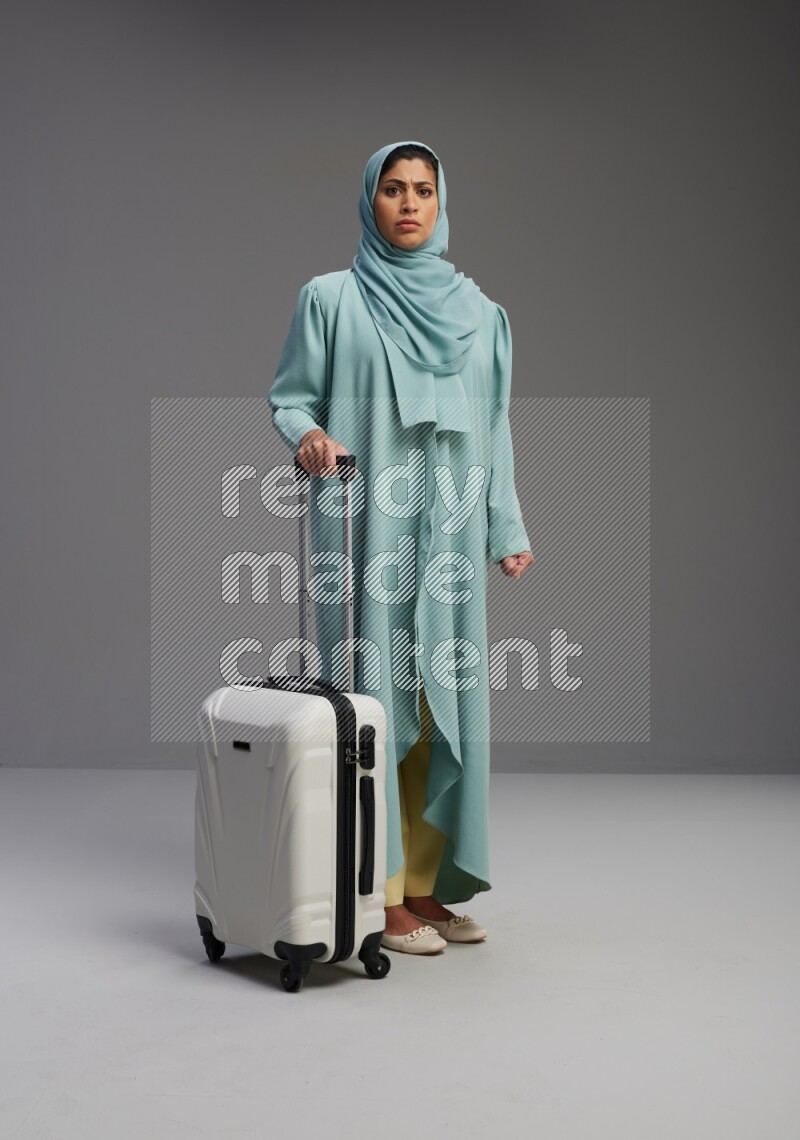 Saudi Woman wearing Abaya standing holding Travel bag on Gray background